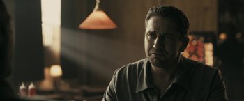 Movie still from “RocknRolla” (2008), directed by Guy Ritchie – A person sitting in front of a lamp; Close Up shot, Over the shoulder angle
