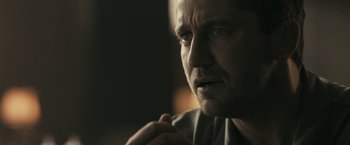 Movie still from “RocknRolla” (2008), directed by Guy Ritchie – A man's face in a dimly - lit room; Close Up shot, Over the shoulder angle