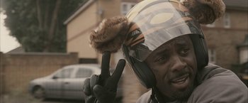 Movie still from “RocknRolla” (2008), directed by Guy Ritchie – A man wearing a motorcycle helmet and gloves; Close Up shot, Over the shoulder angle