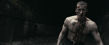 Movie still from “RocknRolla” (2008), directed by Guy Ritchie – A man with a tattoo on his chest and a face; Medium shot, High angle