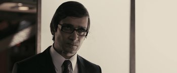 Movie still from “RocknRolla” (2008), directed by Guy Ritchie – A person wearing glasses and a suit; Close Up shot, Over the shoulder angle