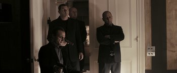 Movie still from “RocknRolla” (2008), directed by Guy Ritchie – A group of men standing next to each other in front of a door; Medium shot, Over the shoulder angle