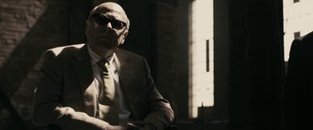 Movie still from “RocknRolla” (2008), directed by Guy Ritchie – An older man wearing a suit and tie; Medium shot, Low angle