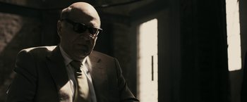 Movie still from “RocknRolla” (2008), directed by Guy Ritchie – An older man wearing a suit and tie; Medium shot, Over the shoulder angle