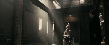 Movie still from “RocknRolla” (2008), directed by Guy Ritchie – A man sitting on top of a chair next to a woman; Wide shot, Low angle