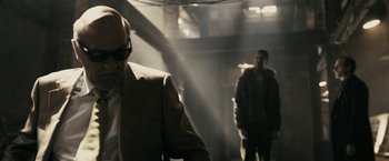 Movie still from “RocknRolla” (2008), directed by Guy Ritchie – A man in a suit and sunglasses standing in front of another man in a jacket; Medium shot, Over the shoulder angle