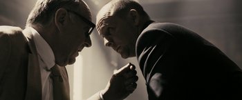 Movie still from “RocknRolla” (2008), directed by Guy Ritchie – Two men are facing each other and one has his arm around the other's elbow; Close Up shot, Over the shoulder angle