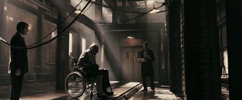 Movie still from “RocknRolla” (2008), directed by Guy Ritchie – A man in a suit and tie standing next to a man in a wheelchair; Wide shot, Low angle