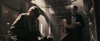 Movie still from “RocknRolla” (2008), directed by Guy Ritchie – A man sitting in front of another man in a dark room; Medium shot, Over the shoulder angle