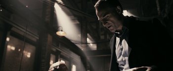 Movie still from “RocknRolla” (2008), directed by Guy Ritchie – A man in a suit and tie standing next to another man; Medium shot, Low angle