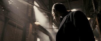 Movie still from “RocknRolla” (2008), directed by Guy Ritchie – A man wearing a suit and tie standing in a building; Medium shot, Low angle
