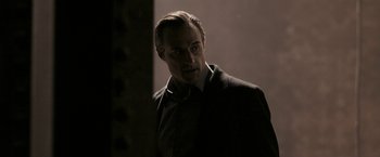 Movie still from “RocknRolla” (2008), directed by Guy Ritchie – A man in a suit standing in front of a wall; Medium shot, Low angle