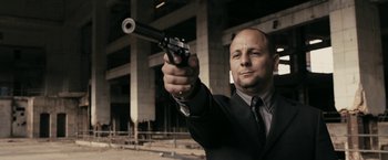 Movie still from “RocknRolla” (2008), directed by Guy Ritchie – A man in a suit and tie holding a gun in his hand; Medium shot, Low angle