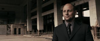 Movie still from “RocknRolla” (2008), directed by Guy Ritchie – A man wearing a suit and tie standing in front of a building; Close Up shot, Low angle