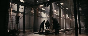 Movie still from “RocknRolla” (2008), directed by Guy Ritchie – A group of men standing around a man laying on the ground; Extreme Wide shot, High angle