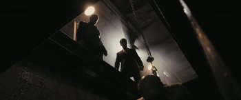 Movie still from “RocknRolla” (2008), directed by Guy Ritchie – Two men are walking up stairs in the dark; Wide shot, Low angle