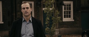 Movie still from “RocknRolla” (2008), directed by Guy Ritchie – A person wearing a suit and tie; Close Up shot, Over the shoulder angle