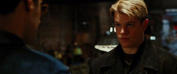 Movie still from “Rounders” (1998), directed by John Dahl – A man with blonde hair is standing in a dark room; Close Up shot, Over the shoulder angle