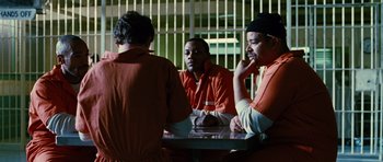Movie still from “Rounders” (1998), directed by John Dahl – A group of men in orange jumpsuits sitting at a table; Medium shot, Over the shoulder angle