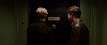 Movie still from “Rounders” (1998), directed by John Dahl – Two men standing next to each other in front of an elevator; Medium shot, High angle