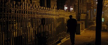 Movie still from “Rounders” (1998), directed by John Dahl – A man walking down a street near a fence; Wide shot, Low angle