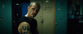 Movie still from “Run All Night” (2015), directed by Jaume Collet-Serra – A man with tattoos is standing next to a door; Close Up shot, Low angle