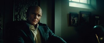 Movie still from “Run All Night” (2015), directed by Jaume Collet-Serra – An older man sitting in a chair in front of a painting; Close Up shot, Over the shoulder angle