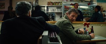 Movie still from “Run All Night” (2015), directed by Jaume Collet-Serra – A man sitting at a counter in front of a bar; Medium shot, Over the shoulder angle