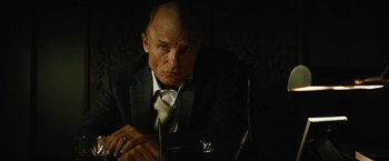 Movie still from “Run All Night” (2015), directed by Jaume Collet-Serra – A man in a suit and tie sitting at a table; Close Up shot, Low angle
