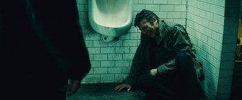 Movie still from “Run All Night” (2015), directed by Jaume Collet-Serra – A man leaning against a urinal on the ground; Medium shot, Over the shoulder angle