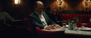 Movie still from “Run All Night” (2015), directed by Jaume Collet-Serra – A man sitting at a table in front of a glass of wine; Medium shot, Low angle