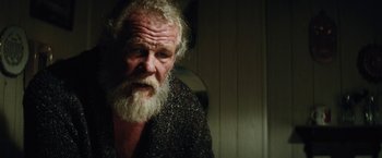 Movie still from “Run All Night” (2015), directed by Jaume Collet-Serra – An old man with a beard is sitting in a room; Close Up shot, Over the shoulder angle