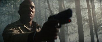 Movie still from “Run All Night” (2015), directed by Jaume Collet-Serra – A man is holding a gun in the woods; Close Up shot, Low angle