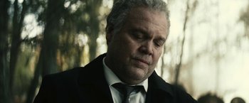 Movie still from “Run All Night” (2015), directed by Jaume Collet-Serra – An older man wearing a suit and tie in front of trees; Close Up shot, Low angle