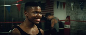 Movie still from “Run All Night” (2015), directed by Jaume Collet-Serra – A young man smiles in front of other people; Close Up shot, Over the shoulder angle
