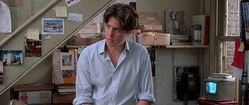 Movie still from “Notting Hill” (1999), directed by Roger Michell – A man in a blue dress shirt is sitting in a room; Medium shot, Over the shoulder angle