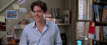 Movie still from “Notting Hill” (1999), directed by Roger Michell – A man smiling while standing in front of a shelf; Close Up shot, Low angle