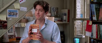 Movie still from “Notting Hill” (1999), directed by Roger Michell – A man in a blue dress shirt holding a book; Close Up shot, Over the shoulder angle