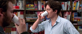 Movie still from “Notting Hill” (1999), directed by Roger Michell – A man drinking from a cup in front of a book shelf; Close Up shot, Low angle
