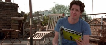 Movie still from “Notting Hill” (1999), directed by Roger Michell – A man sitting on top of a chair holding a magazine; Medium shot, Low angle
