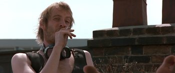 Movie still from “Notting Hill” (1999), directed by Roger Michell – A man smoking a cigarette while sitting on a bench; Close Up shot, Low angle