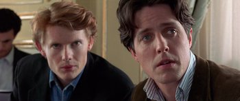 Movie still from “Notting Hill” (1999), directed by Roger Michell – Two men sitting next to each other in front of a wall; Close Up shot, Over the shoulder angle