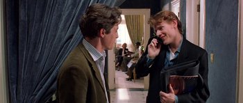 Movie still from “Notting Hill” (1999), directed by Roger Michell – Two men talking on a cell phone in front of a crowd; Medium shot, Over the shoulder angle