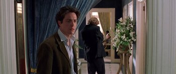 Movie still from “Notting Hill” (1999), directed by Roger Michell – A man standing in a room holding a flower in his hand; Medium shot, Over the shoulder angle