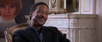 Movie still from “Notting Hill” (1999), directed by Roger Michell – A man sitting in a chair in front of a fireplace; Close Up shot, Over the shoulder angle