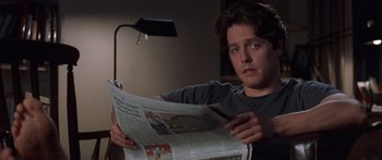 Movie still from “Notting Hill” (1999), directed by Roger Michell – A man sitting down reading a newspaper in the dark; Close Up shot, Over the shoulder angle