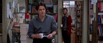 Movie still from “Notting Hill” (1999), directed by Roger Michell – A man standing next to another man in a room; Medium shot, Over the shoulder angle
