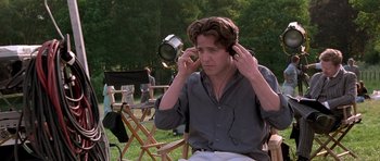 Movie still from “Notting Hill” (1999), directed by Roger Michell – A man in a field listening to music with headphones; Medium shot, Over the shoulder angle