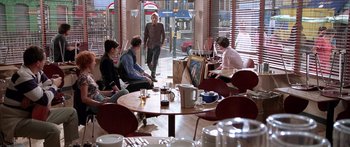Movie still from “Notting Hill” (1999), directed by Roger Michell – A group of people sitting at tables in a restaurant; Wide shot, Over the shoulder angle