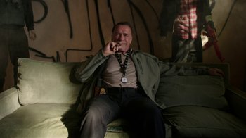 Movie still from “Sabotage” (2014), directed by David Ayer – A man sitting on top of a couch with a medal around his neck; Medium shot, Low angle